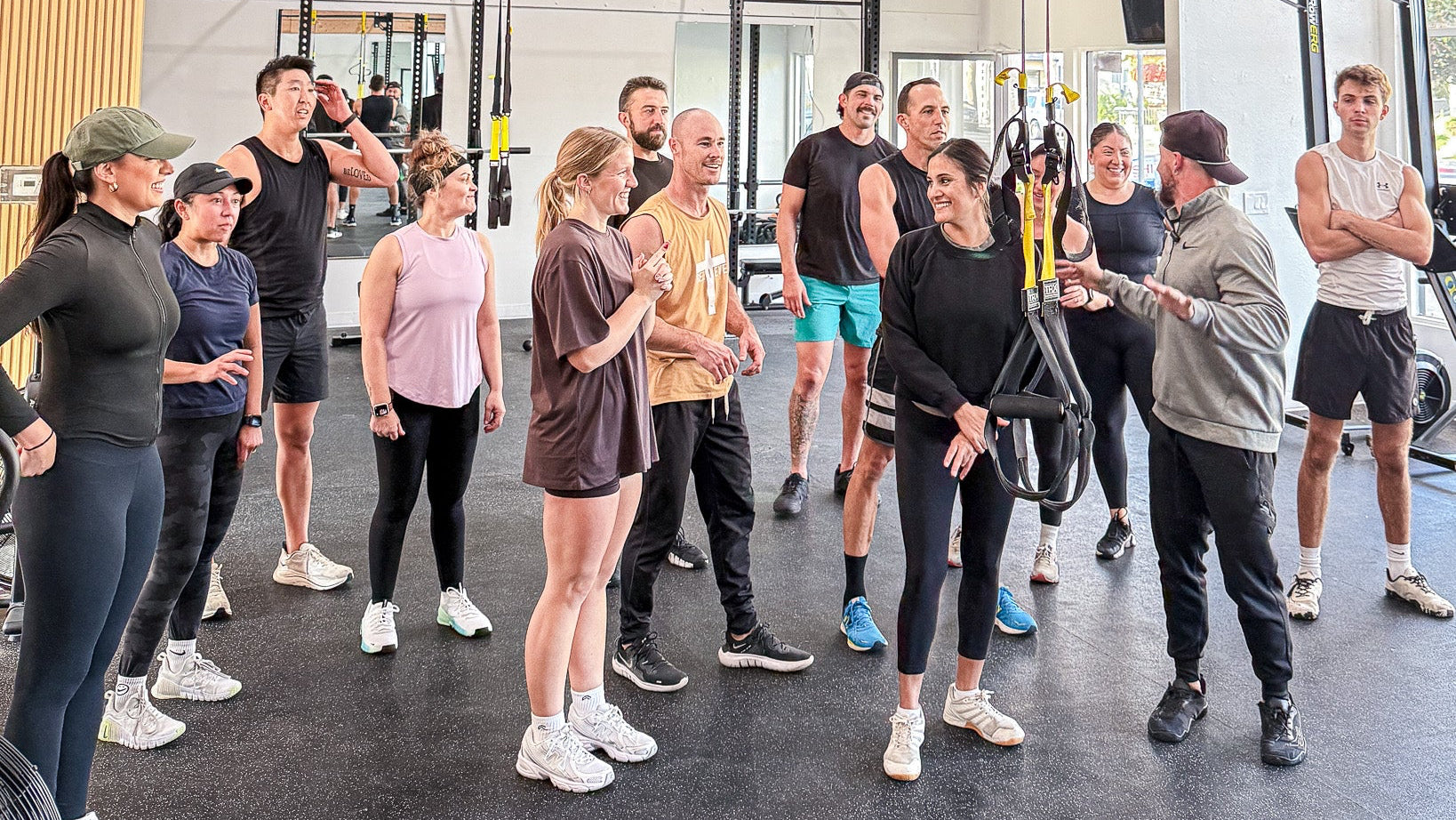 Group of people in a fitness studio with TRX suspension training equipment.